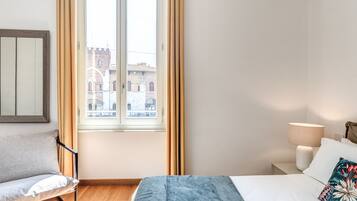 Un dormitorio con cama, mesita de noche, lámpara, silla y ventana con cortinas.