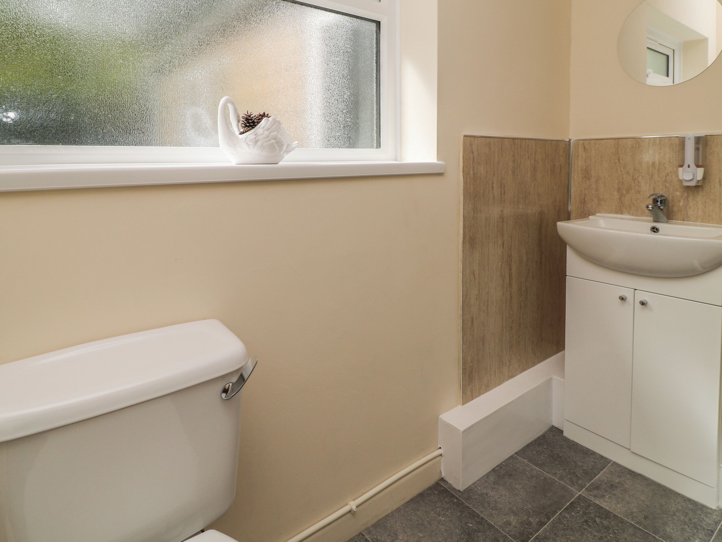 A bathroom with a toilet, a sink, and a window with a decorative item.