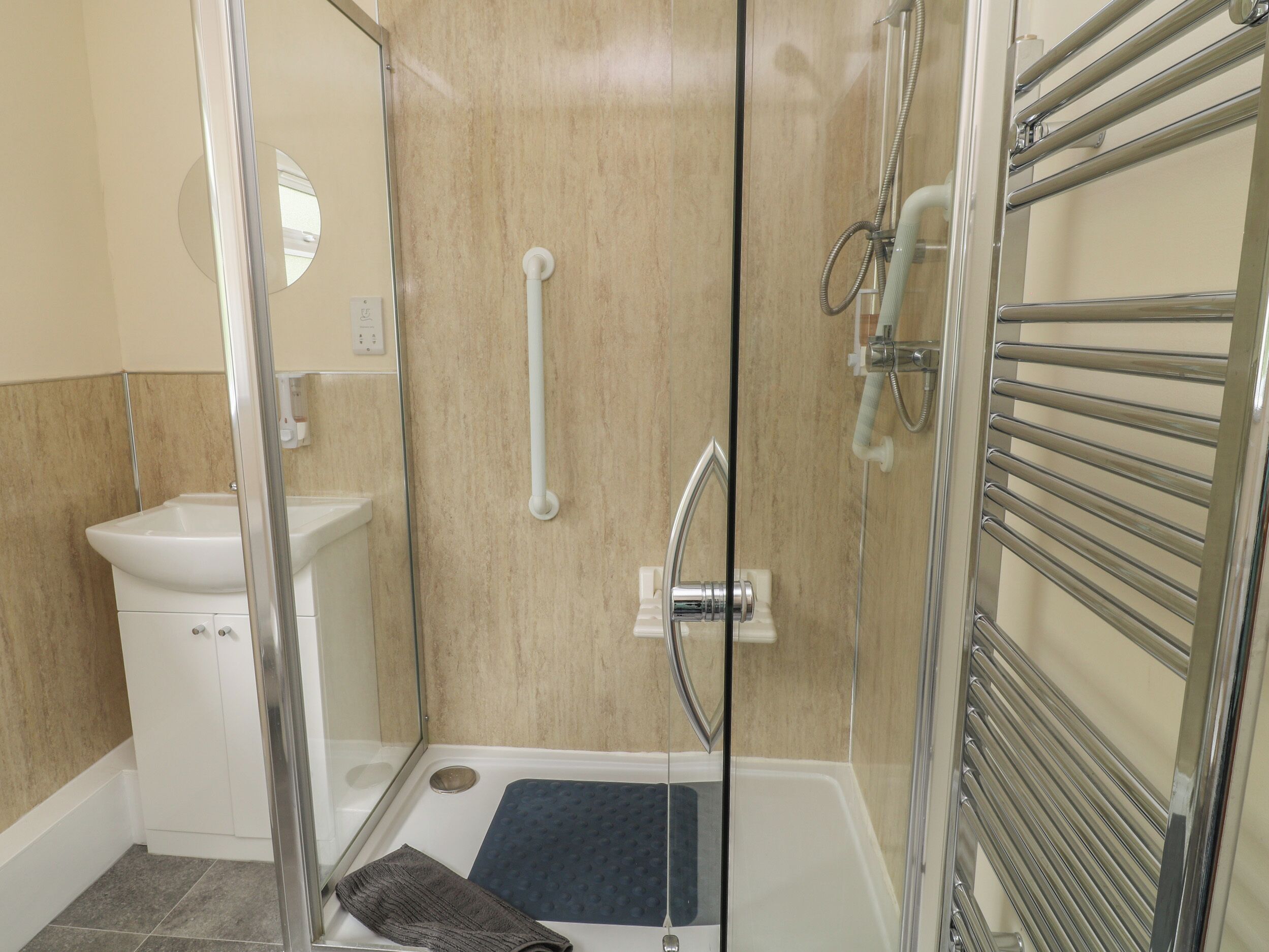 Un baño moderno con ducha acristalada, un lavabo blanco y un perchero para toallas.