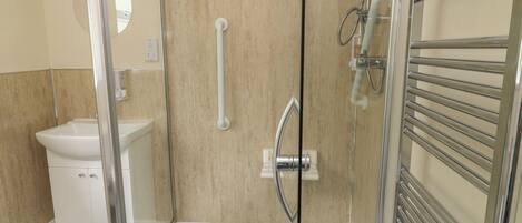 Un baño moderno con ducha acristalada, un lavabo blanco y un perchero para toallas.