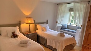 A hotel room with two beds, a nightstand with a lamp, a window with a view, and a wooden wardrobe.