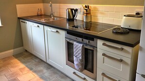 A modern kitchen with white cabinets, a black countertop, a built-in oven, and a kettle.