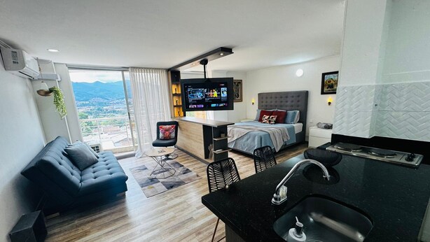 Un appartement moderne comprenant un espace de vie, une chambre, une kitchenette et une grande fenêtre donnant sur la ville.