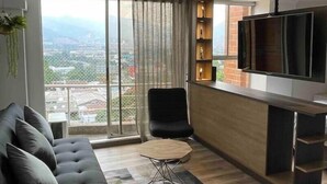 Un salon moderne avec un canapé, une table basse, un téléviseur et une vue sur le paysage urbain grâce à de grandes fenêtres.