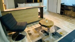 Un salon moderne avec un canapé, un fauteuil noir, une table basse et un téléviseur fixé au mur.