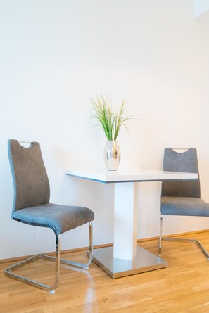 Une pièce moderne avec deux fauteuils gris à revêtement en tissu, une table blanche, une plante en pot et un plancher en bois.