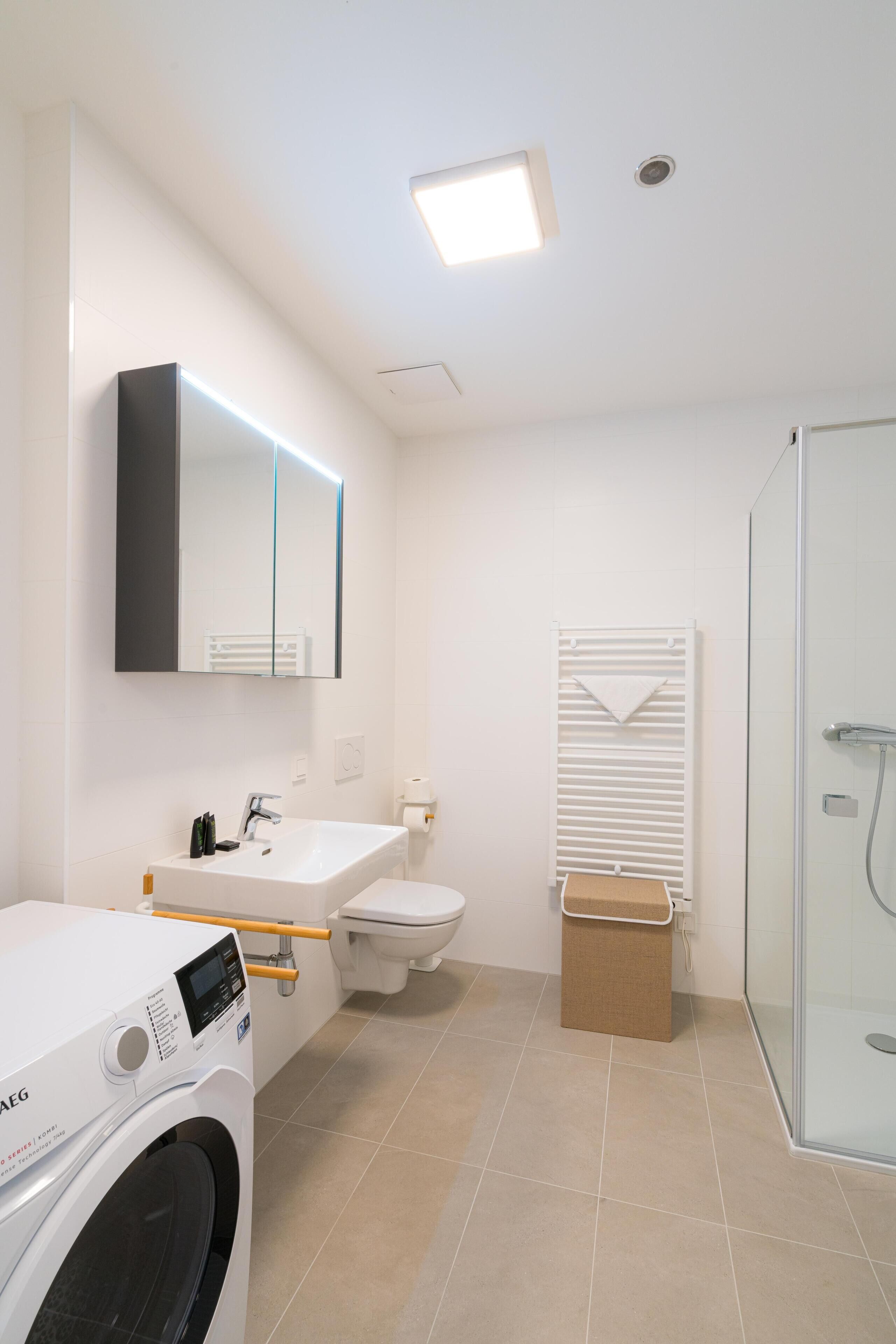 Un baño moderno con lavadora, lavabo, inodoro y cabina de ducha de cristal.