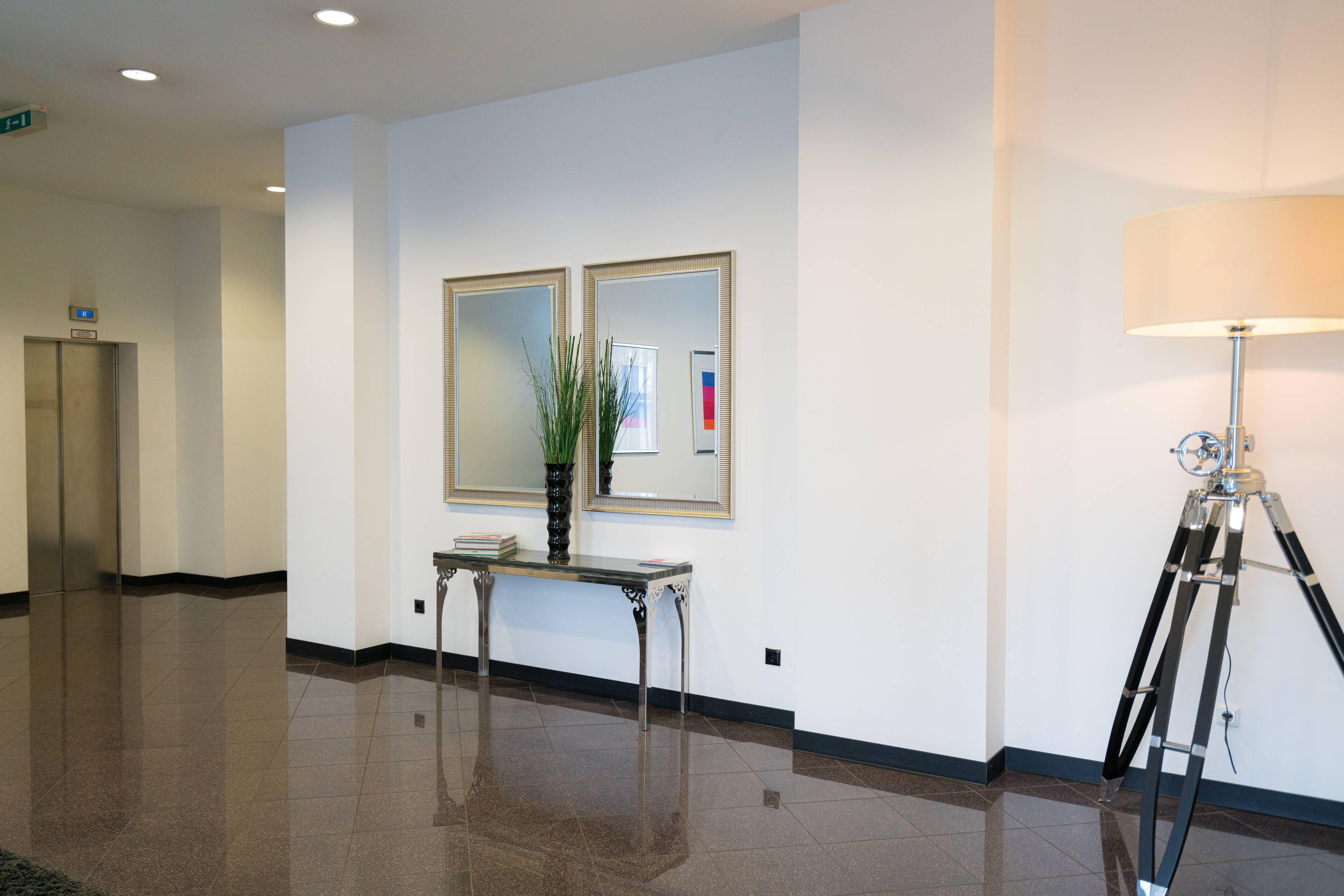 A hallway with a polished floor, a mirror, a lamp, and a small table with a plant.