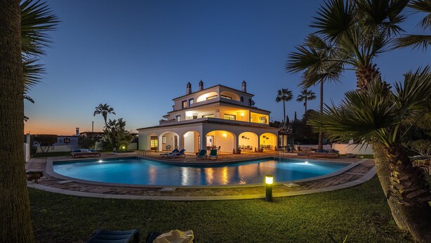 A two-story house with a swimming pool, surrounded by palm trees and a well-lit patio area. - Flat Buganvilia OCV - Pool & Private Parking (Albufeira)