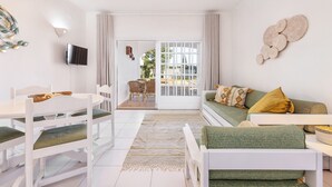 A modern living room with a dining area, a sofa with cushions, a flat-screen TV, and a decorative wall piece. - Flat Buganvilia OCV - Pool & Private Parking (Albufeira)