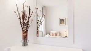 A white bathroom with a large mirror, a vase with dried flowers, and a framed picture on the wall. - Flat Buganvilia OCV - Pool & Private Parking (Albufeira)
