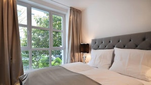 A hotel room with a large window, a tufted headboard, and a bedside lamp. - Vienna Residence, Frankfurt - Schweizer Platz #6070 (Frankfurt)