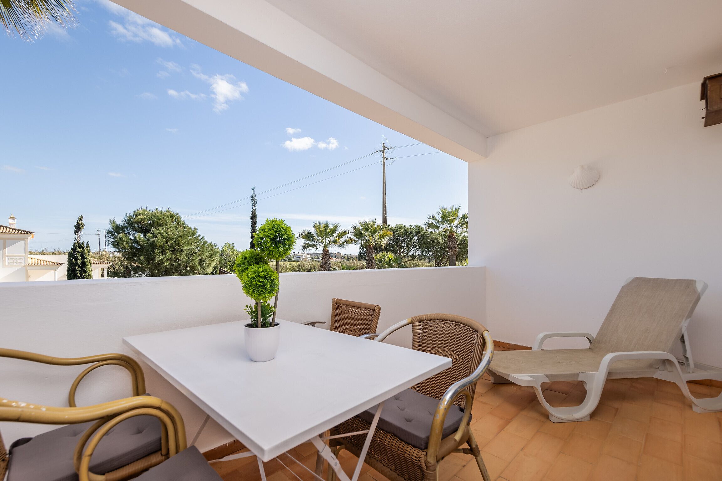 A balcony with a white table, wicker chairs, and a potted plant.