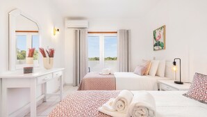 Une chambre d’hôtel avec un grand lit, un plus petit lit, un bureau avec un miroir, une coiffeuse et une fenêtre avec des rideaux.