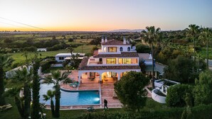 Una casa grande con piscina, rodeada de exuberante follaje y palmeras.