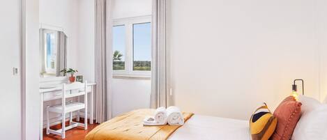 A hotel room with two beds, a desk, and a window with a view.