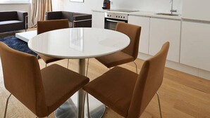 Une cuisine moderne avec des meubles blancs, une table de salle à manger ronde entourée de quatre chaises, et un canapé dans le salon attenant.