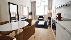 Une chambre d’hôtel compacte comprenant un coin repas, un canapé, une télévision, une cuisine équipée d’une cuisinière et une grande fenêtre avec des rideaux.