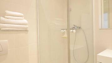 Ein modernes Badezimmer mit einer gläsernen Dusche, einer Toilette und einem Stapel weißer Handtücher.