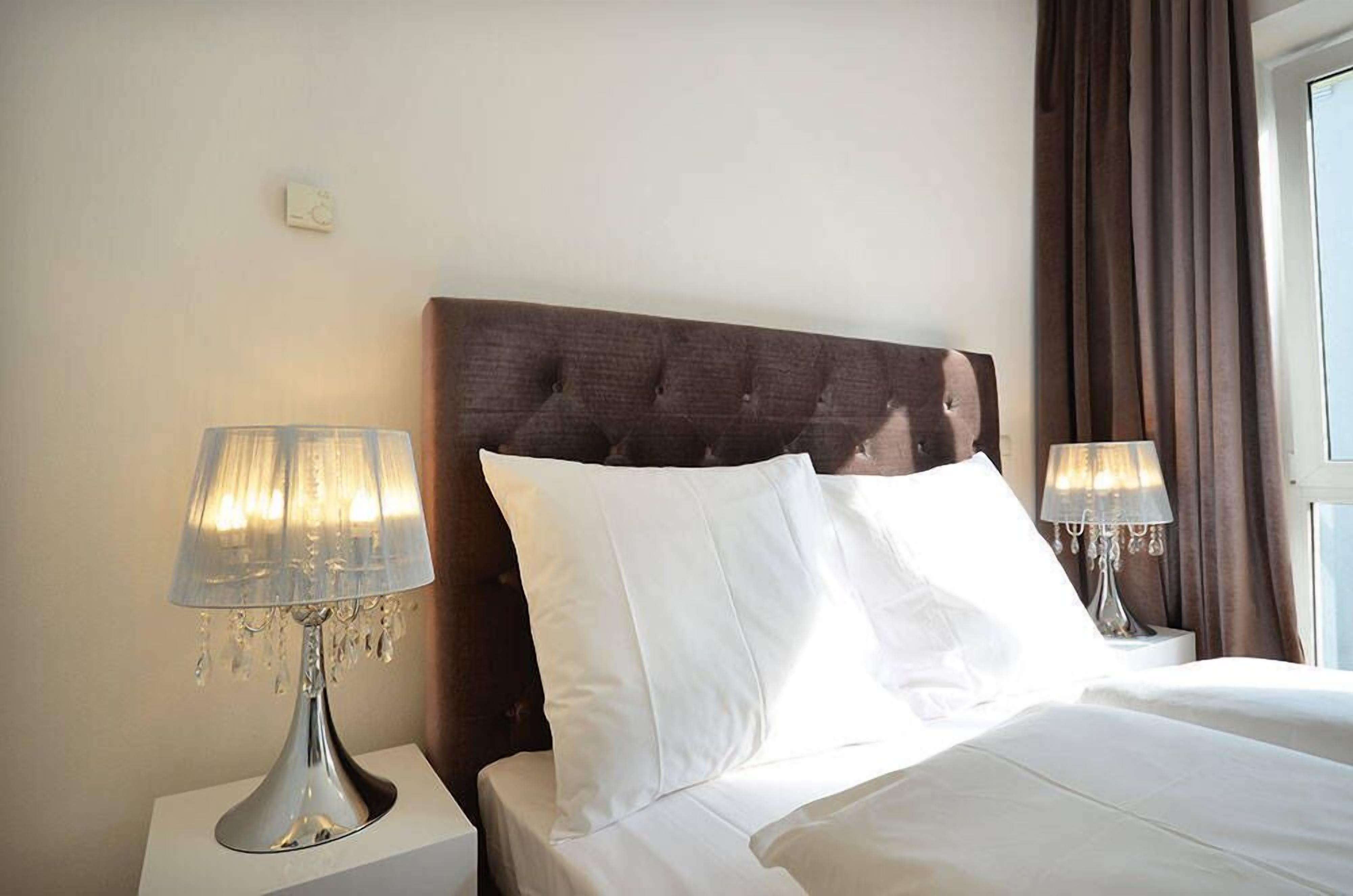 Ein Hotelzimmer mit einem gepolsterten Kopfteil, weißer Bettwäsche und zwei Nachttischlampen.