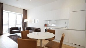 Une cuisine moderne avec des meubles blancs, une table de salle à manger ronde entourée de quatre chaises, et un canapé dans le salon attenant.