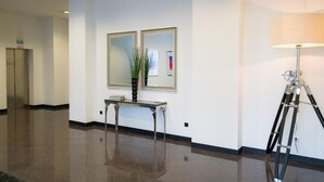Un hall d’entrée propre et moderne, avec un sol ciré, un comptoir d’accueil, un grand miroir et une lampe.