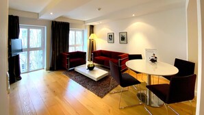 Un salon moderne avec un canapé rouge, une table basse, un téléviseur et un coin repas comprenant une table ronde et des chaises.