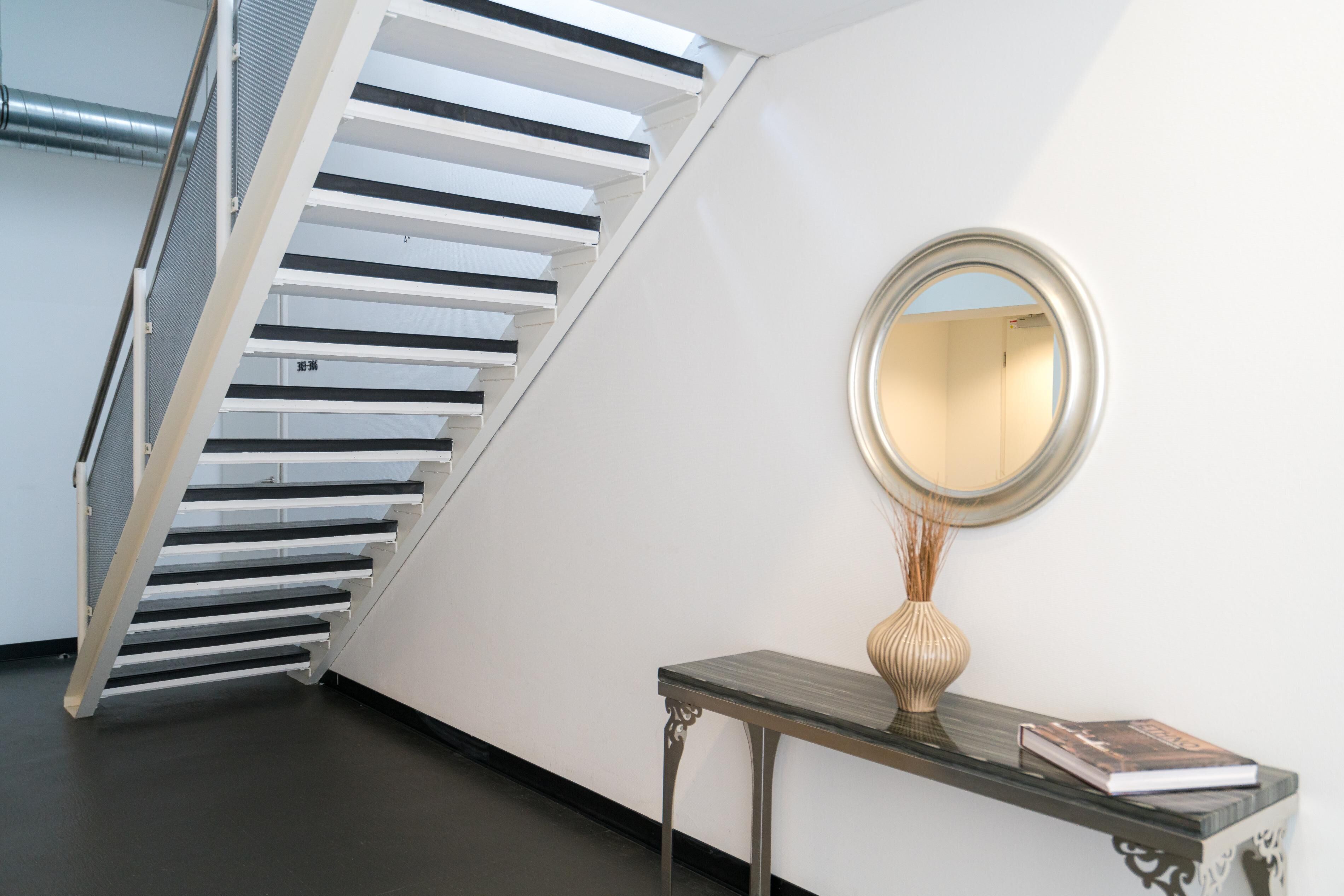 Una escalera con barandillas blancas y un espejo redondo en la pared.