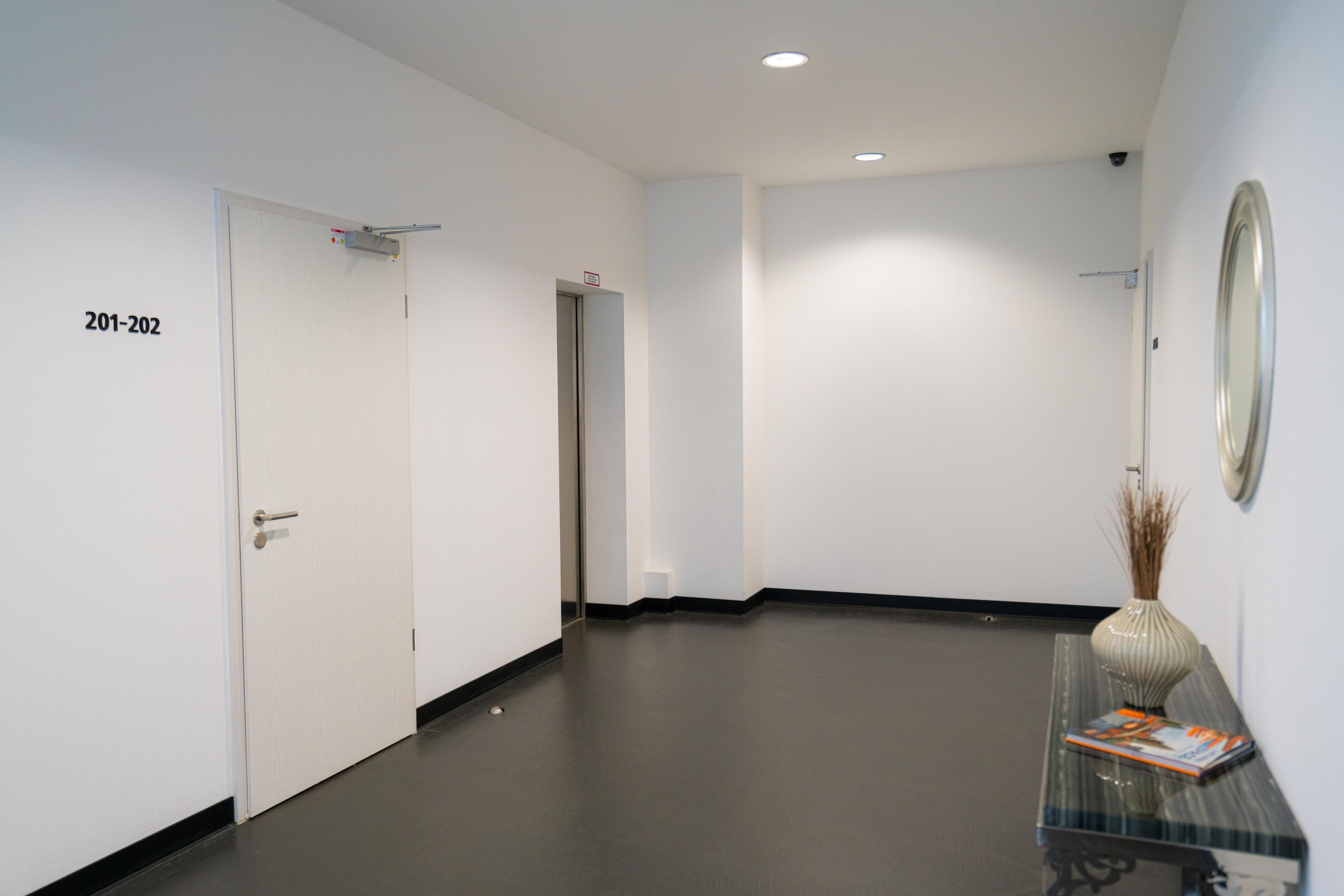 A hallway with a dark floor, white walls, and a door labeled "201-202".