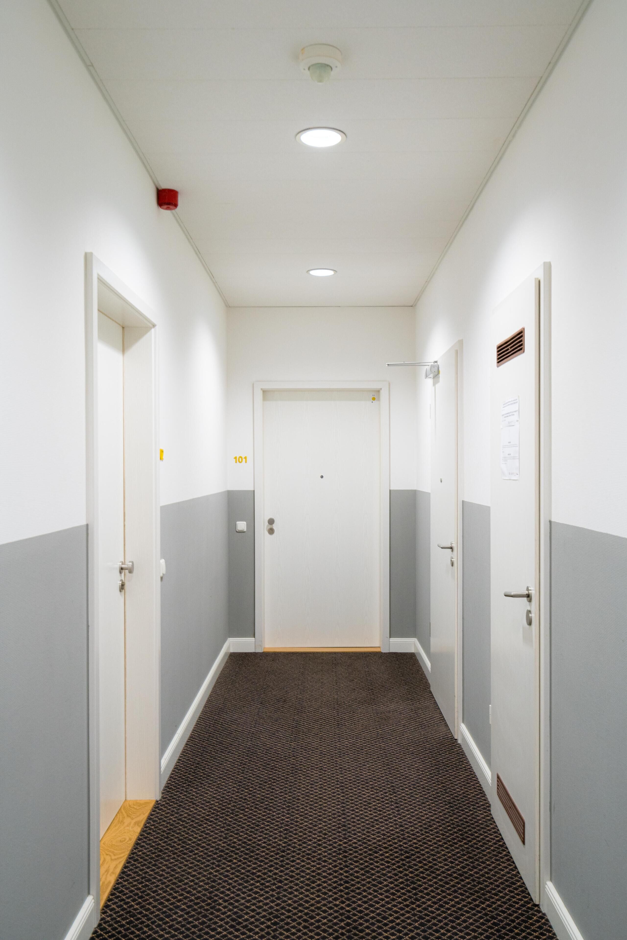 Un couloir étroit, doté d’un tapis à motifs, de murs blancs et de portes numérotées 101 et 102.