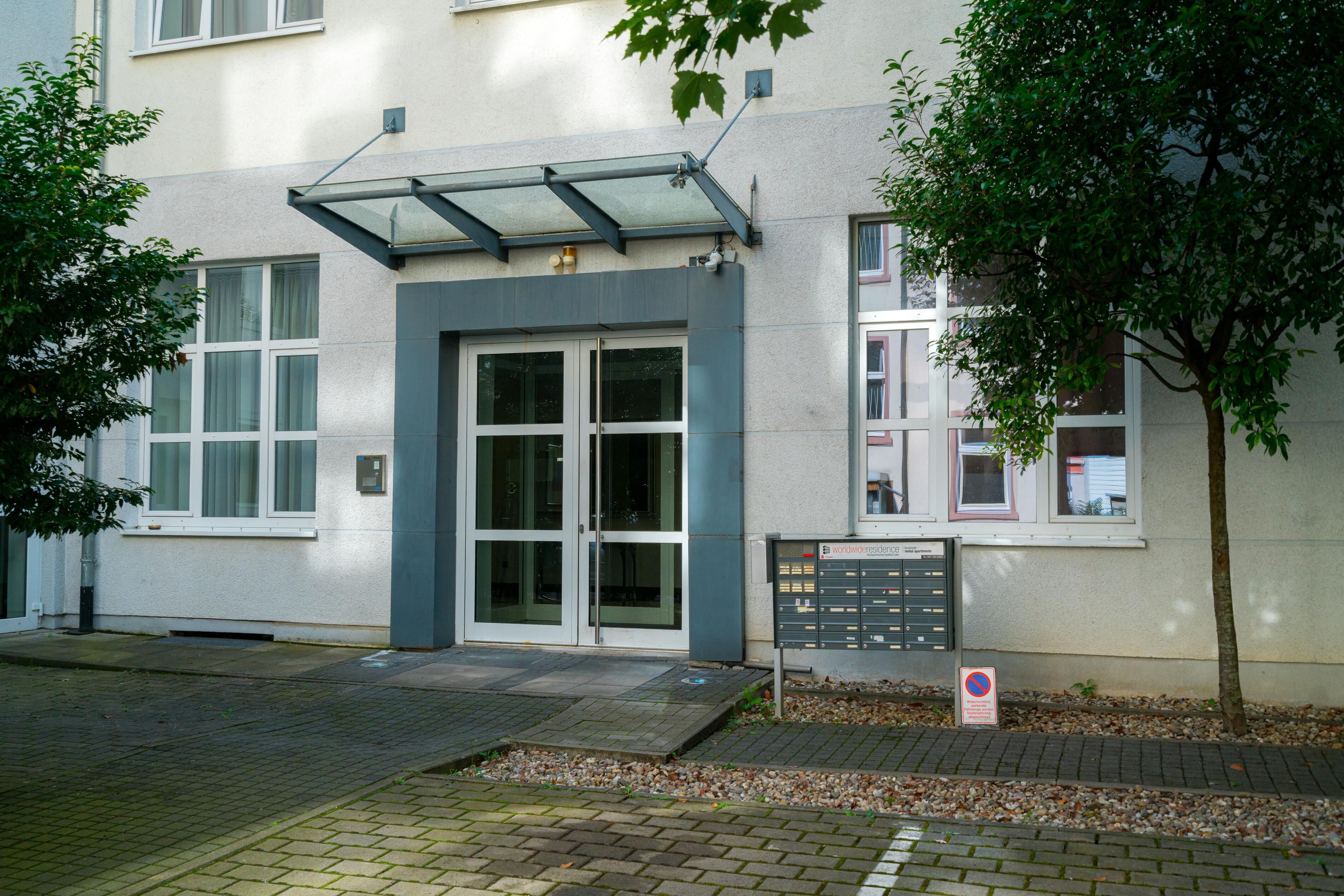 A building with a glass entrance, a metal signboard, and a tree in front.