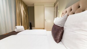 Quarto de hotel com uma cama bem arrumada, uma porta e uma janela com cortinas.