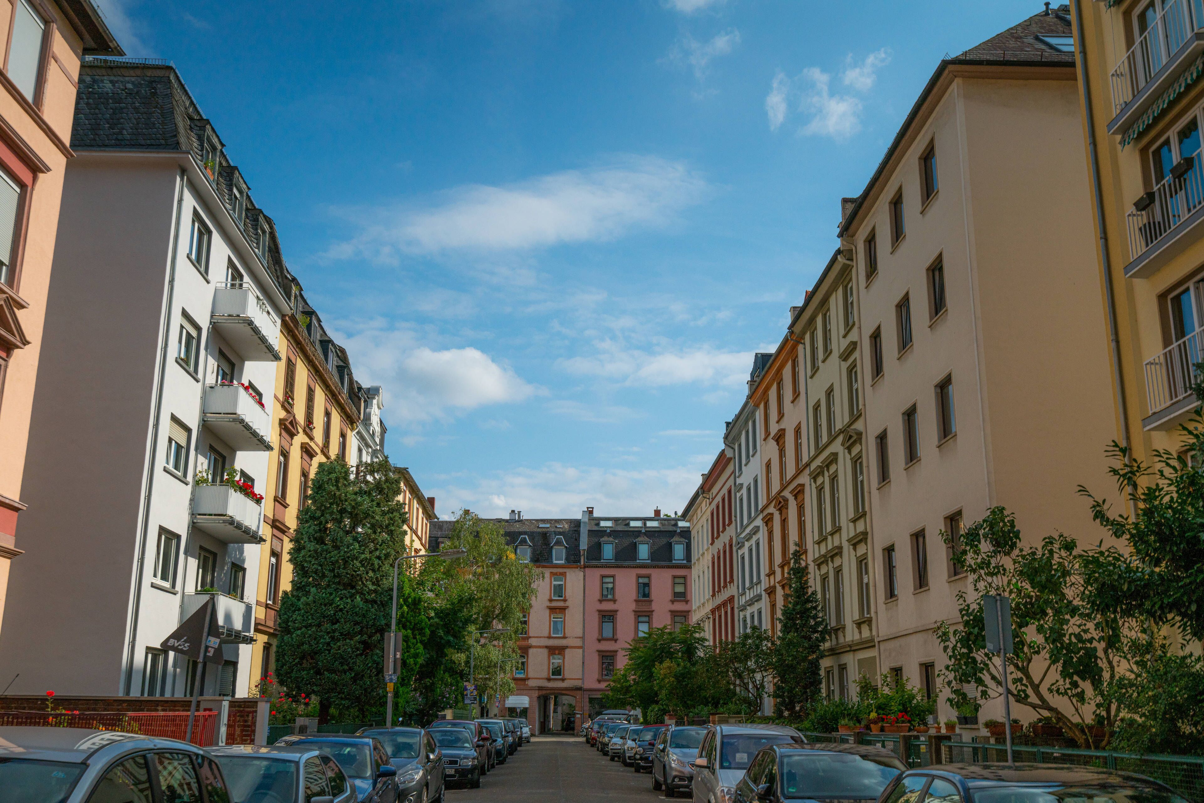 Una vista di strada con edifici a più piani, auto parcheggiate e alberi.
