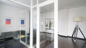A modern room with a glass partition, a grey sofa, a desk with a lamp, and framed artwork on the wall. - Vienna Residence, Frankfurt - Schweizer Platz #6083 (Frankfurt)