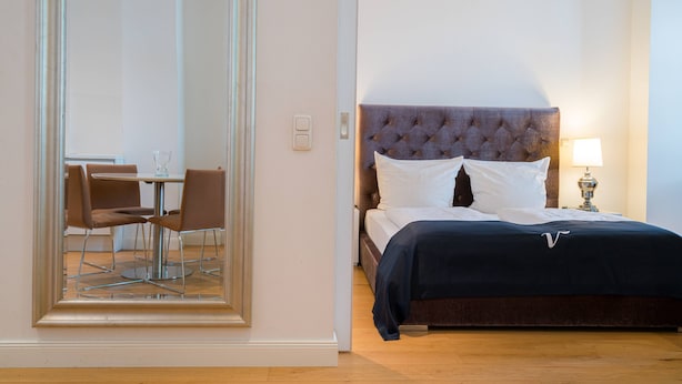 A bedroom with a bed, bedside table, lamp, and a dining area with chairs and a table. - Vienna Residence, Frankfurt - Schweizer Platz #6084 (Frankfurt)