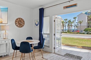 A room with a round table, blue chairs, a wooden clock, a painting, and a view of palm trees and a road outside. - Great Location with Easy Beach Access! (Destin)