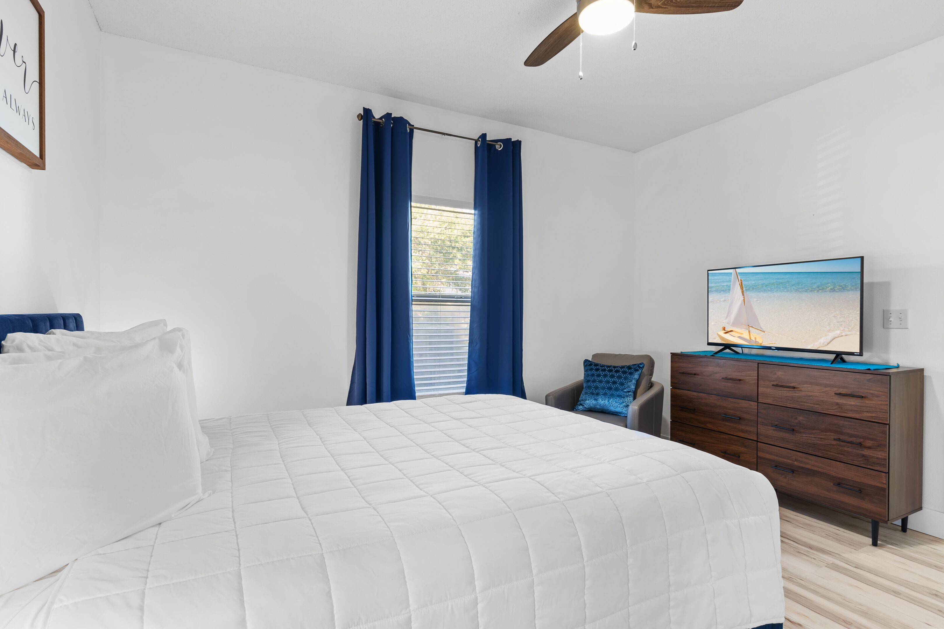 Une chambre à coucher avec un lit, une commode, un téléviseur et une fenêtre avec des rideaux.