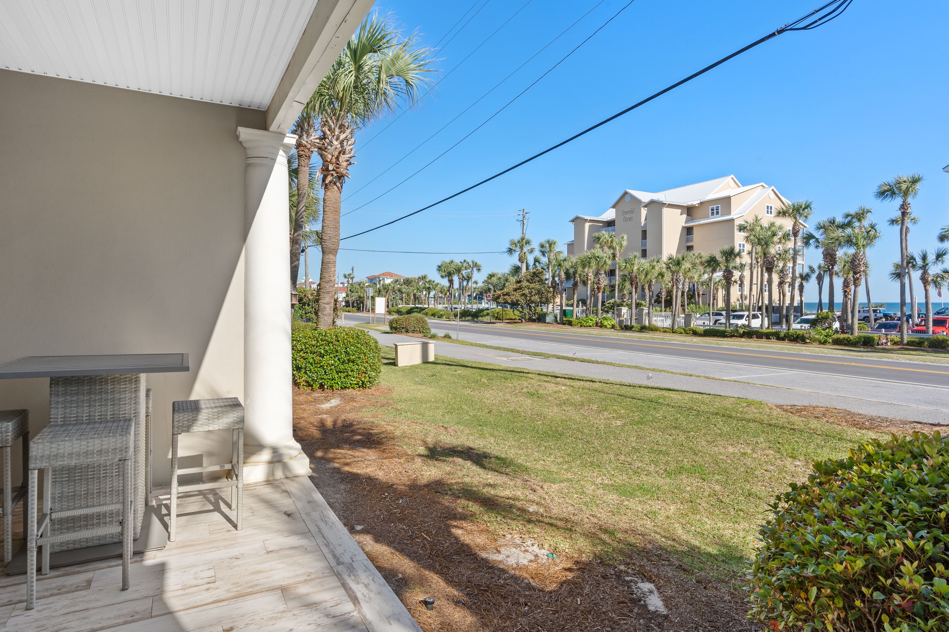 A hotel with a covered outdoor seating area, palm trees, and a road in the background.