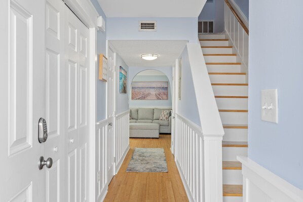 A hallway with white doors, a gray couch, and a staircase with wooden steps.