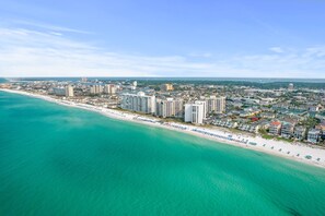 An aerial view of a coastal city with a beach, high-rise buildings, and a clear sky.