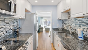 Una cocina moderna con armarios blancos, un refrigerador de acero inoxidable, un microondas y una encimera de granito.