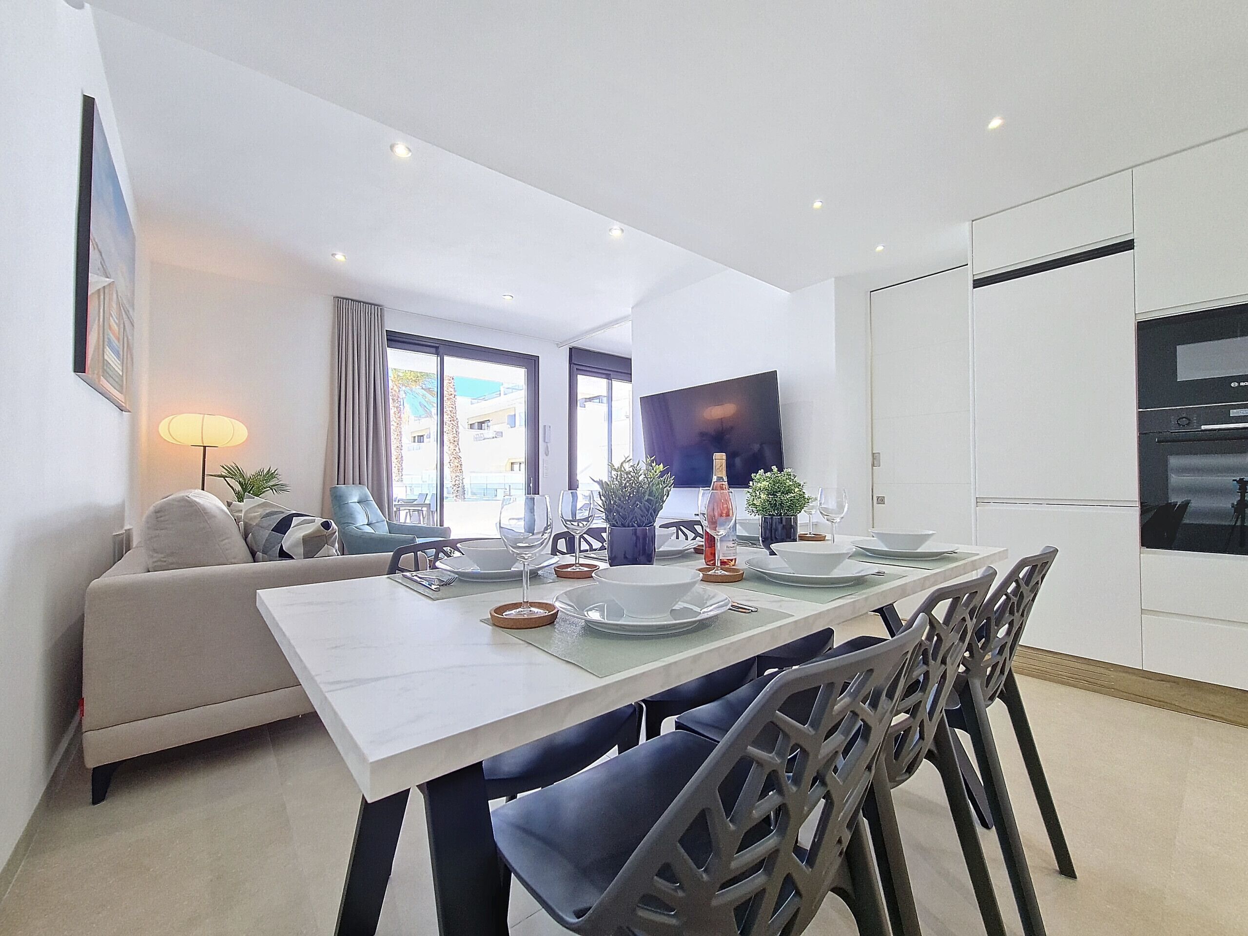 Un comedor moderno con una mesa larga, sillas y un televisor al fondo.