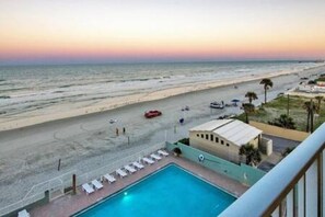 Zona de piscina con vista a la playa y al océano al atardecer.