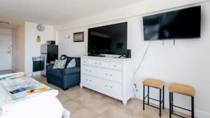 Un dormitorio moderno con cama, cómoda, televisor y dos taburetes.