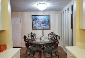 A dining area with a round table and chairs, a painting on the wall, and a door in the background. - 101 Bent Tree Modern Lux 2BR 2BA Heated Pool (Daytona Beach)