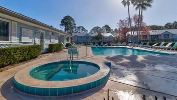 A pool area with a hot tub, lounge chairs, and a building with a covered patio. - 101 Bent Tree Modern Lux 2BR 2BA Heated Pool (Daytona Beach)