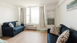 Ein Wohnzimmer mit einem dunkelblauen Sofa, einer weißen Klimaanlage und einem fenster mit Vorhängen.