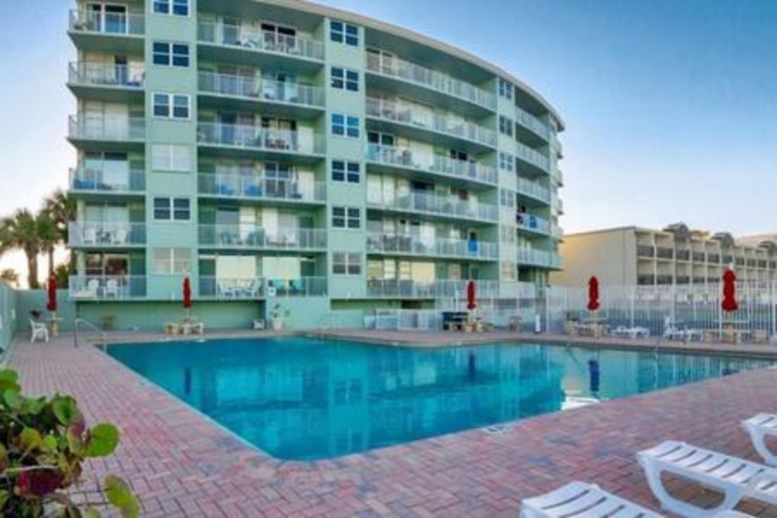 A multi-story hotel with a swimming pool, outdoor seating, and a curved balcony.