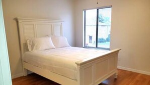 Ein weißes Bett mit Kopfteil in einem Zimmer mit Holzboden und einem Fenster.
