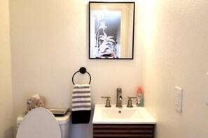 A bathroom with a toilet, sink, and a framed picture above the mirror.